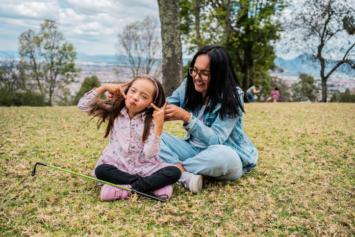Portrait of a child girl with down syndrome playing to mother sitting on the floor outdoors